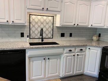 A kitchen with white cabinets , granite counter tops , a sink , and a black dishwasher.