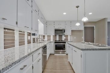 A kitchen with white cabinets , granite counter tops , stainless steel appliances and a large island.