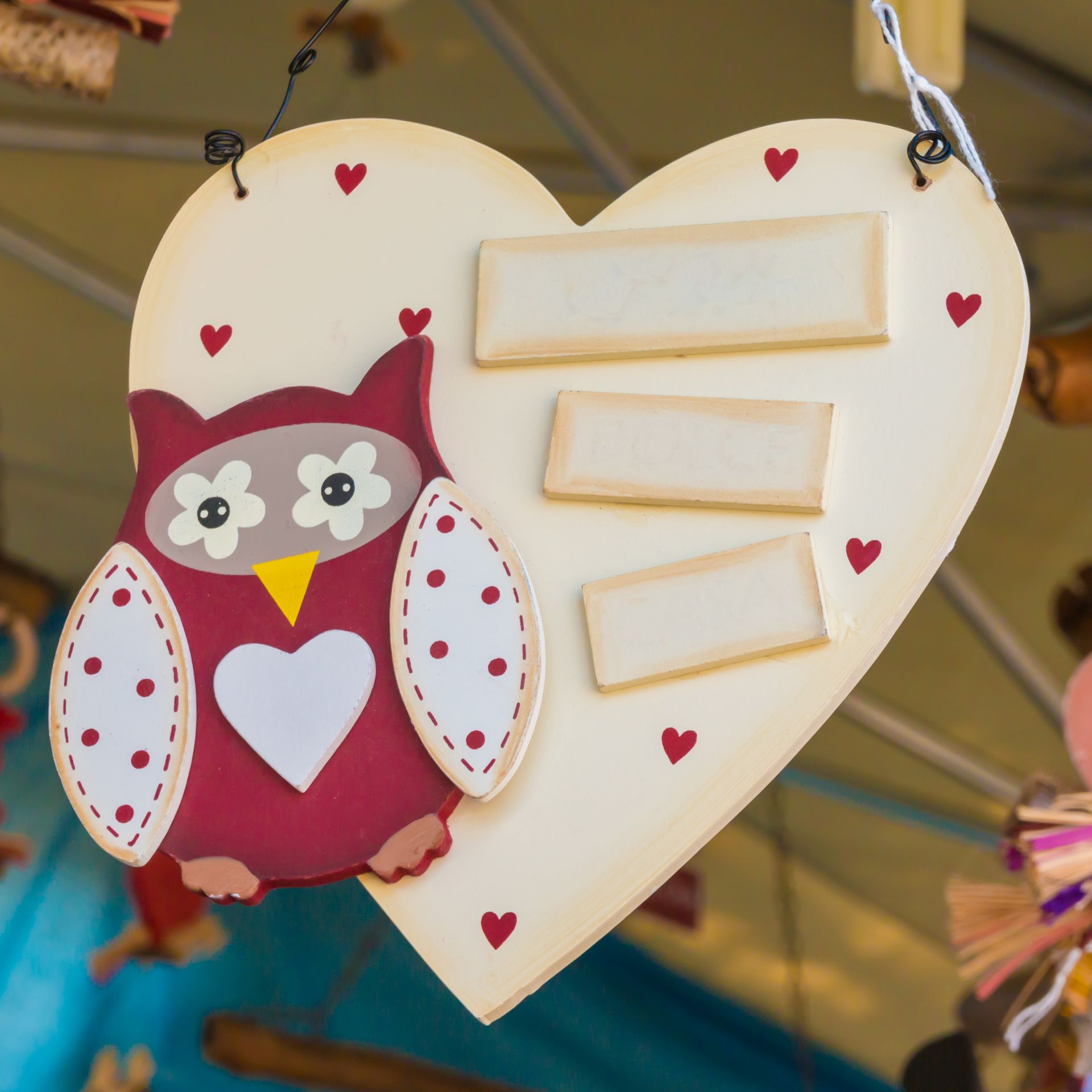 Heart-shaped wooden sign with owl decoration and space for three name tags, red hearts, cream background.
