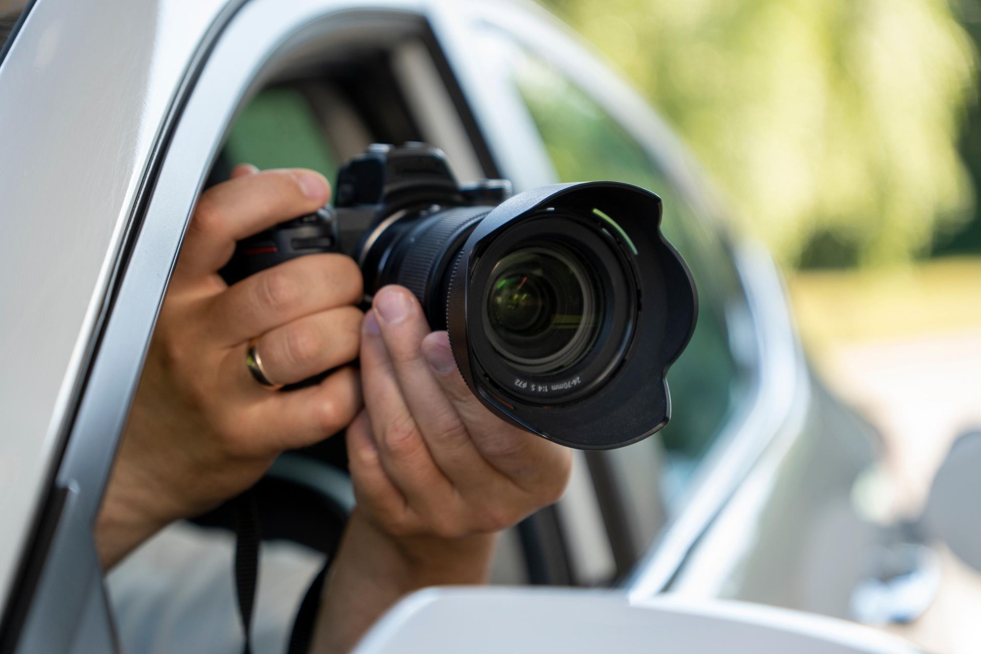Hands holding a camera with a lens, positioned in a car window, likely for photography.