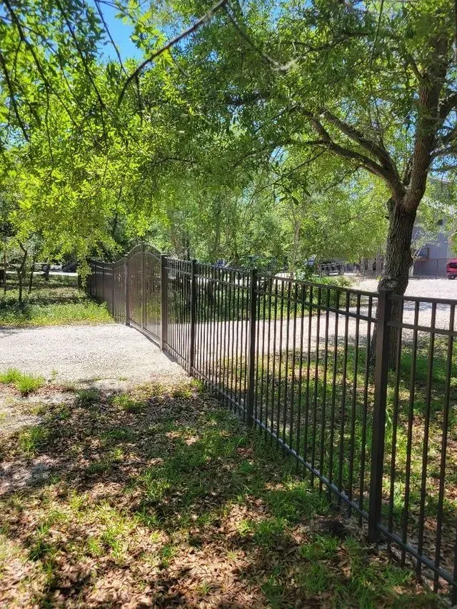 A metal fence is surrounded by trees and grass in a park.