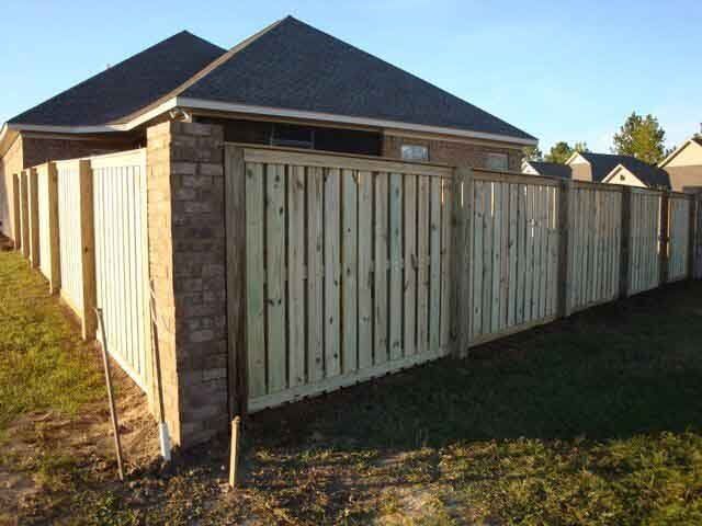 A wooden fence surrounds a brick house in a residential area.