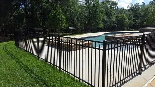 A black fence surrounds a swimming pool in a backyard.
