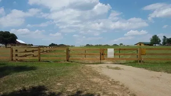A wooden fence surrounds a dirt road in a field.