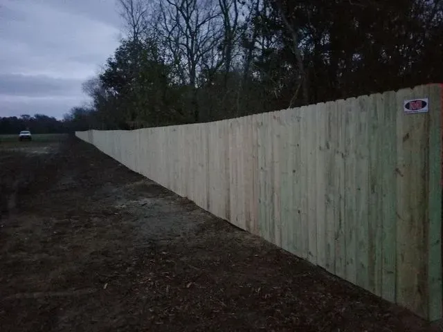 A long wooden fence is sitting on the side of a dirt road.