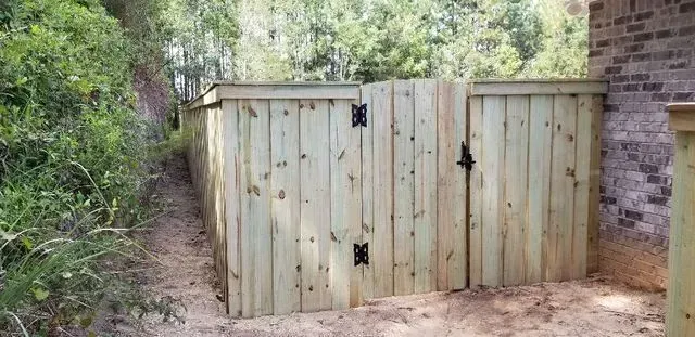 A wooden fence with a gate is surrounded by trees.