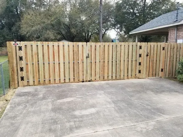 A wooden fence with a gate in a driveway next to a house.