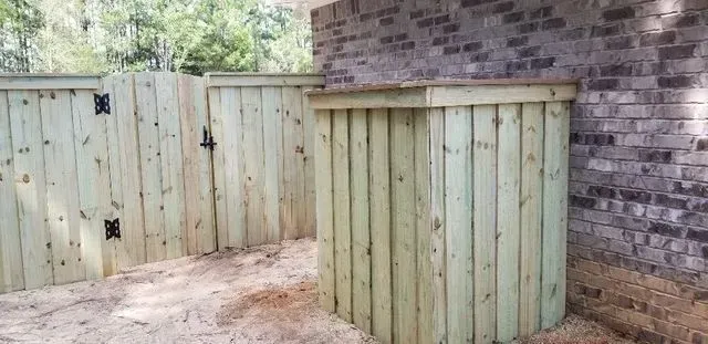 A wooden fence with a gate in front of a brick building.