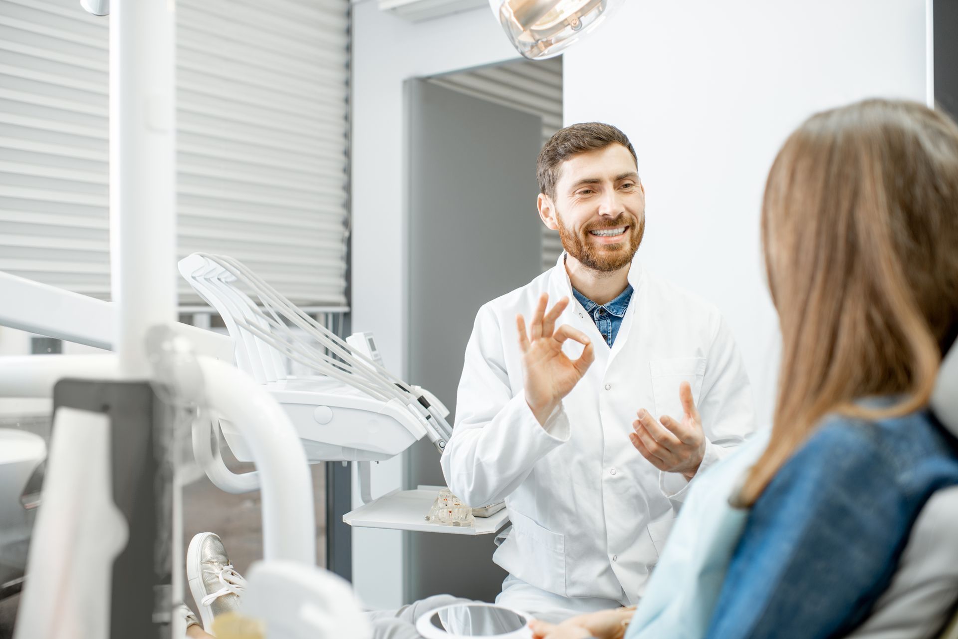 A dentist is giving an okay sign to a patient in a dental chair.