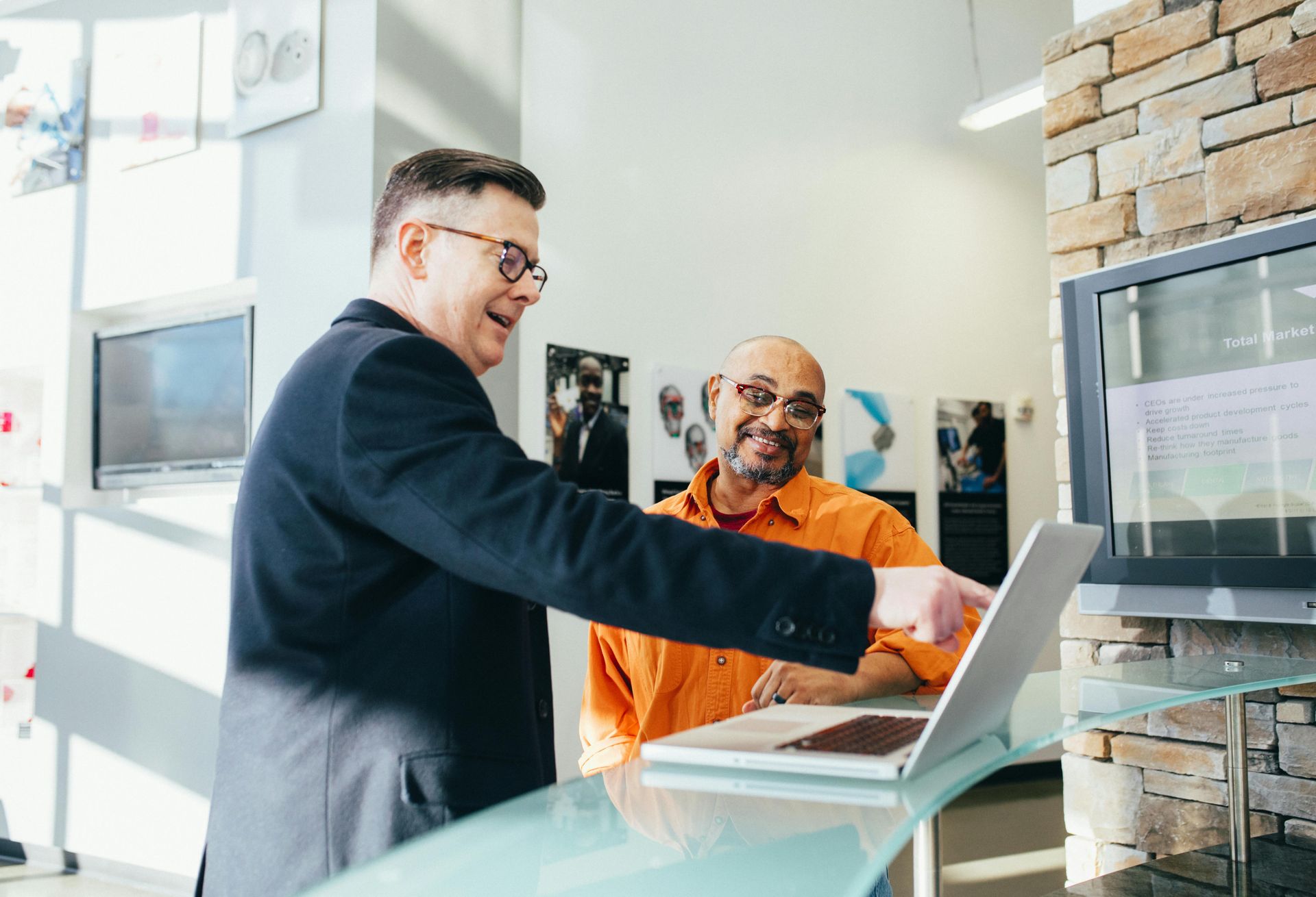 A man is pointing at a laptop computer while another man looks on.