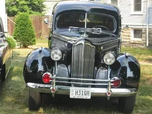 Black classic car with chrome details, parked on grass. The front is visible, with a license plate.