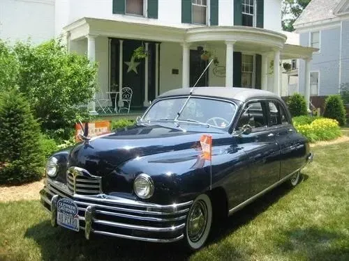 Dark blue Packard car parked on a lawn in front of a white house.