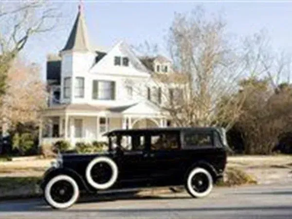 Black antique car parked in front of a white Victorian house.