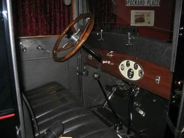 Interior of a vintage car with a wooden steering wheel, dashboard, and black leather seats.