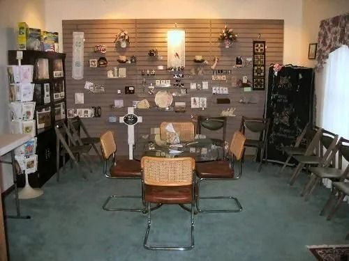 A room with display shelves, chairs, and a table, likely a funeral home's visitation area.