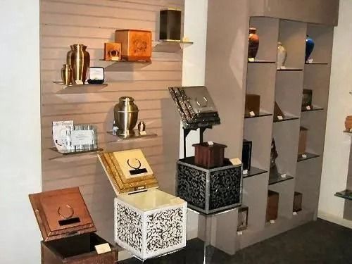 Display of cremation urns in a shop. Various sizes, shapes, and materials are featured on shelves and display cubes.