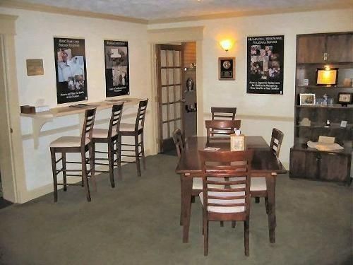 A room with a bar, dining table, chairs, and display cabinet. Posters hang on the walls.