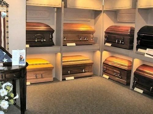 Display of various caskets in a funeral home. Wooden and metal caskets on display shelves.