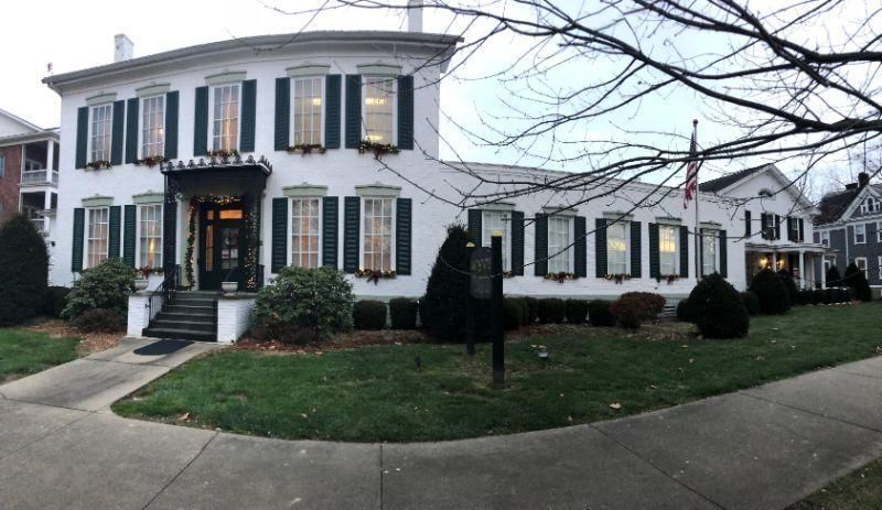 White two-story building with green shutters, black awning, and flagpole on a lawn.