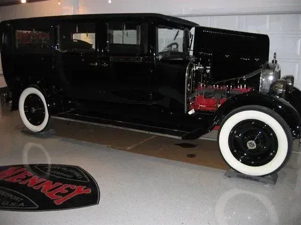 Black vintage sedan with white-wall tires, parked in a garage. Hood open, exposing the engine.