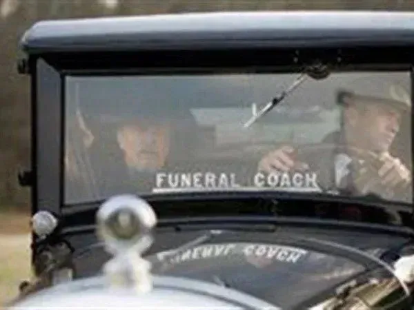 Black vintage funeral coach with driver and passenger.