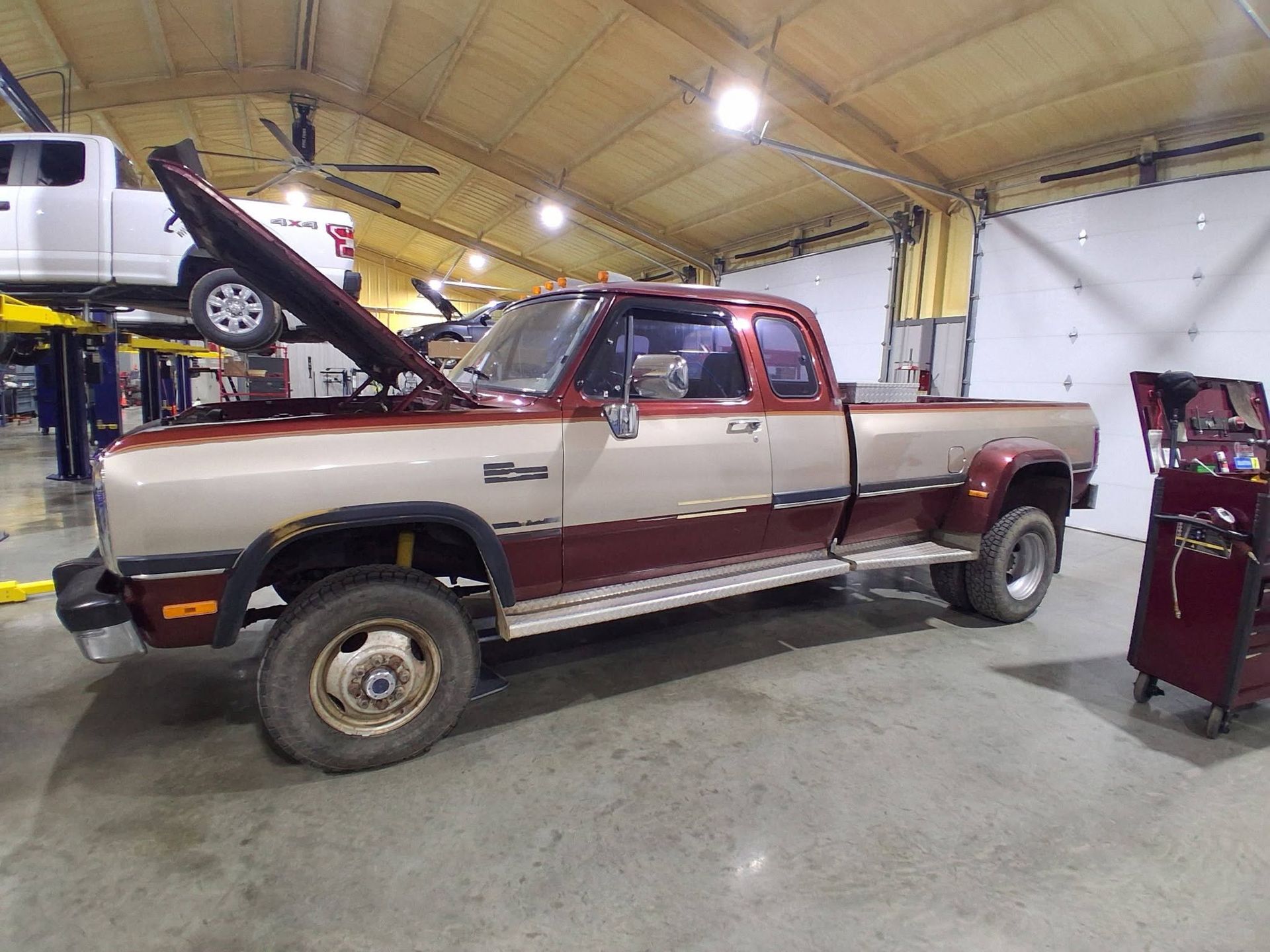 Two-tone pickup truck with open hood inside a garage or workshop, showing the side view.