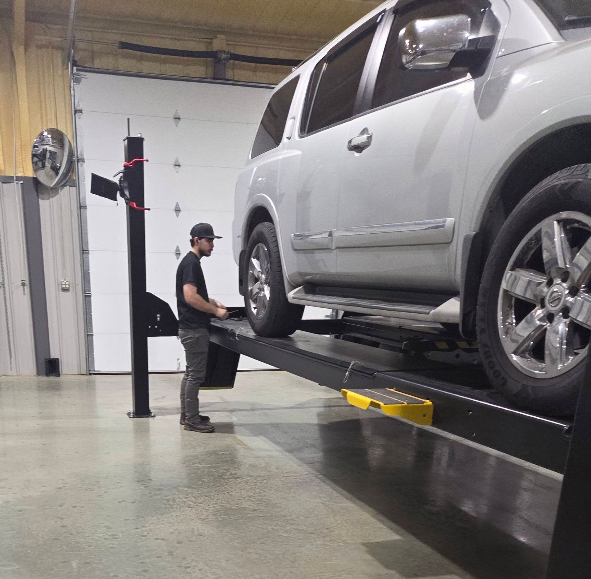 Mechanic inspecting a silver SUV on a hydraulic lift in an auto repair shop