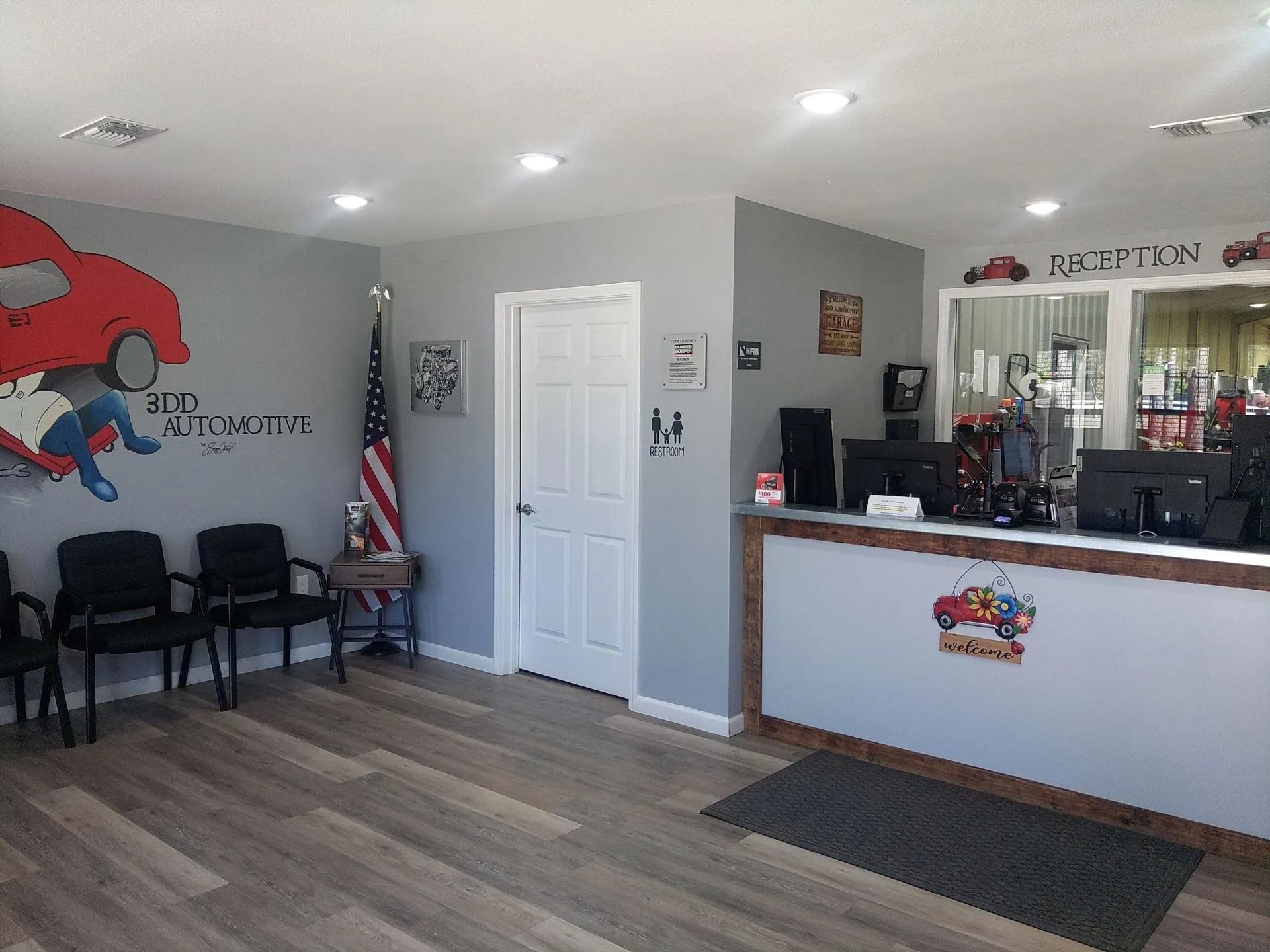 Bright auto shop waiting area with chairs, counter, American flag, and car mural on the wall.