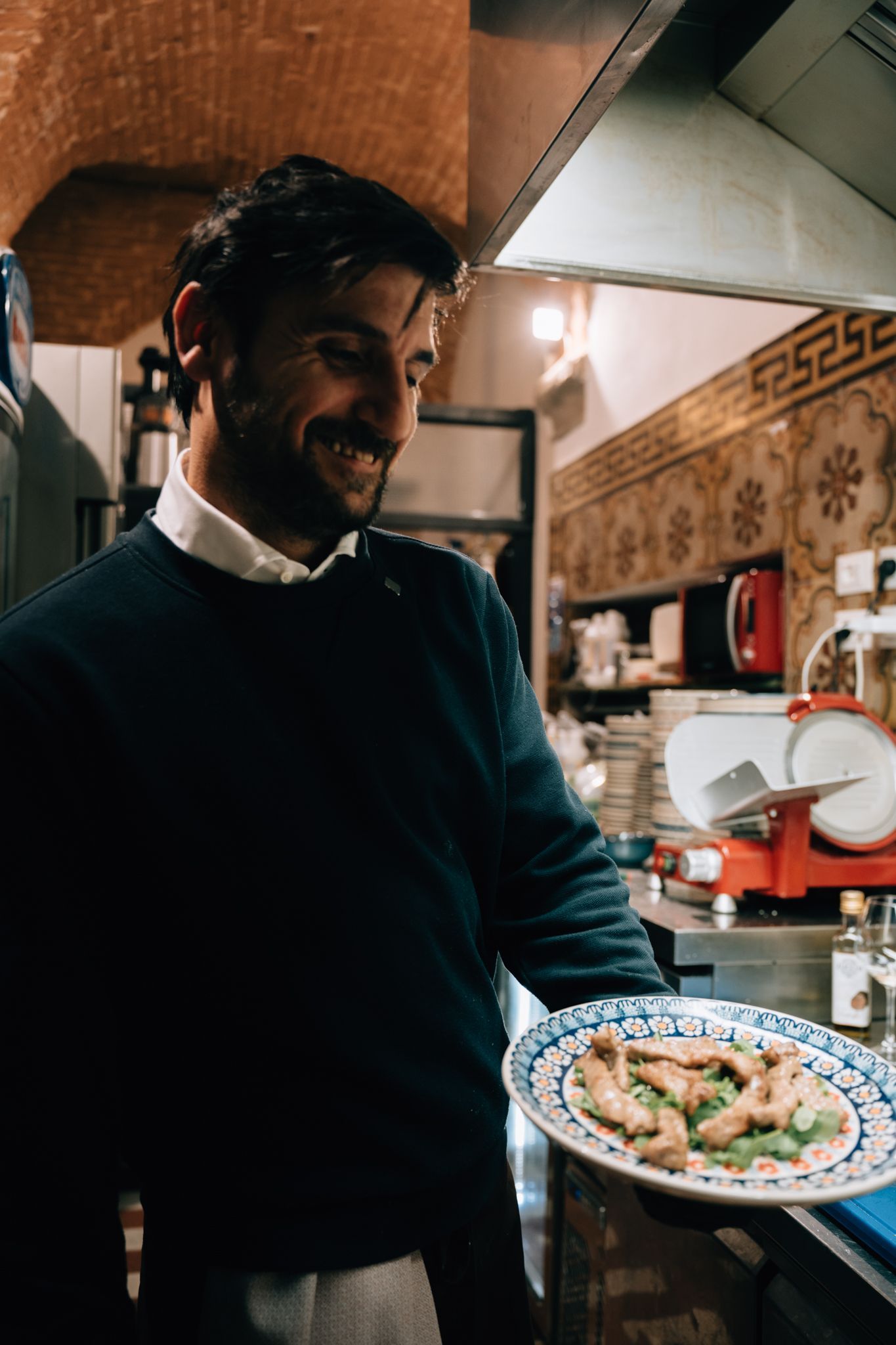 Uno chef sorridente tiene in mano un piatto di cibo nella cucina di un ristorante.