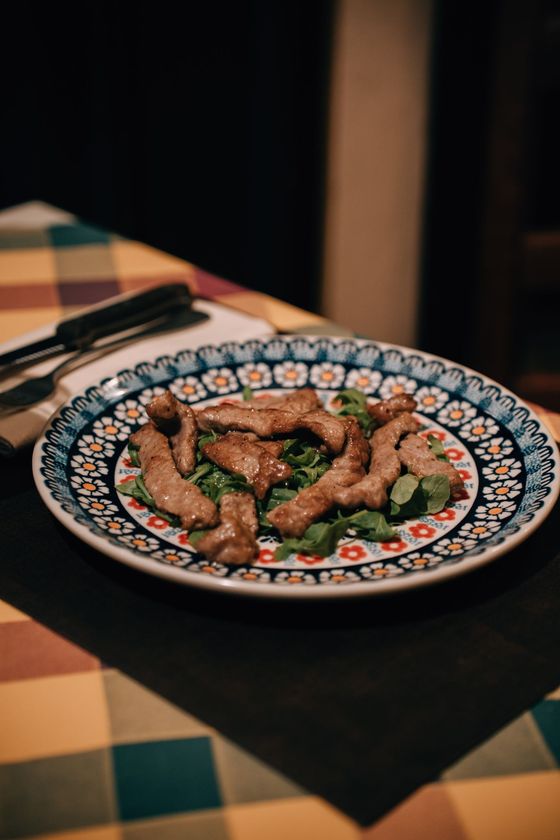 Piatto di striscioline di carne su rucola, su un piatto decorato, su una tovaglia a quadretti con posate.