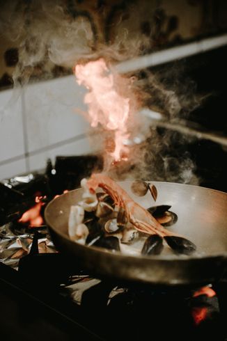 Padella di frutti di mare sul fuoco durante la cottura. Le fiamme salgono, il vapore fuoriesce dalla padella.