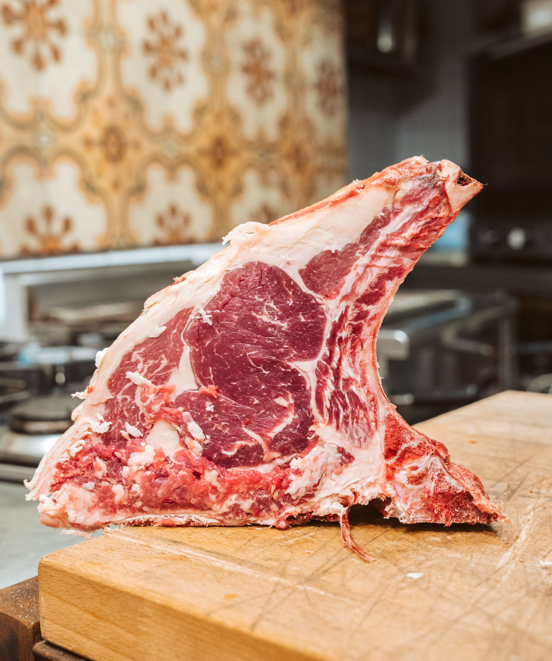 Grande bistecca di ribeye cruda su un tagliere di legno, sullo sfondo della cucina.