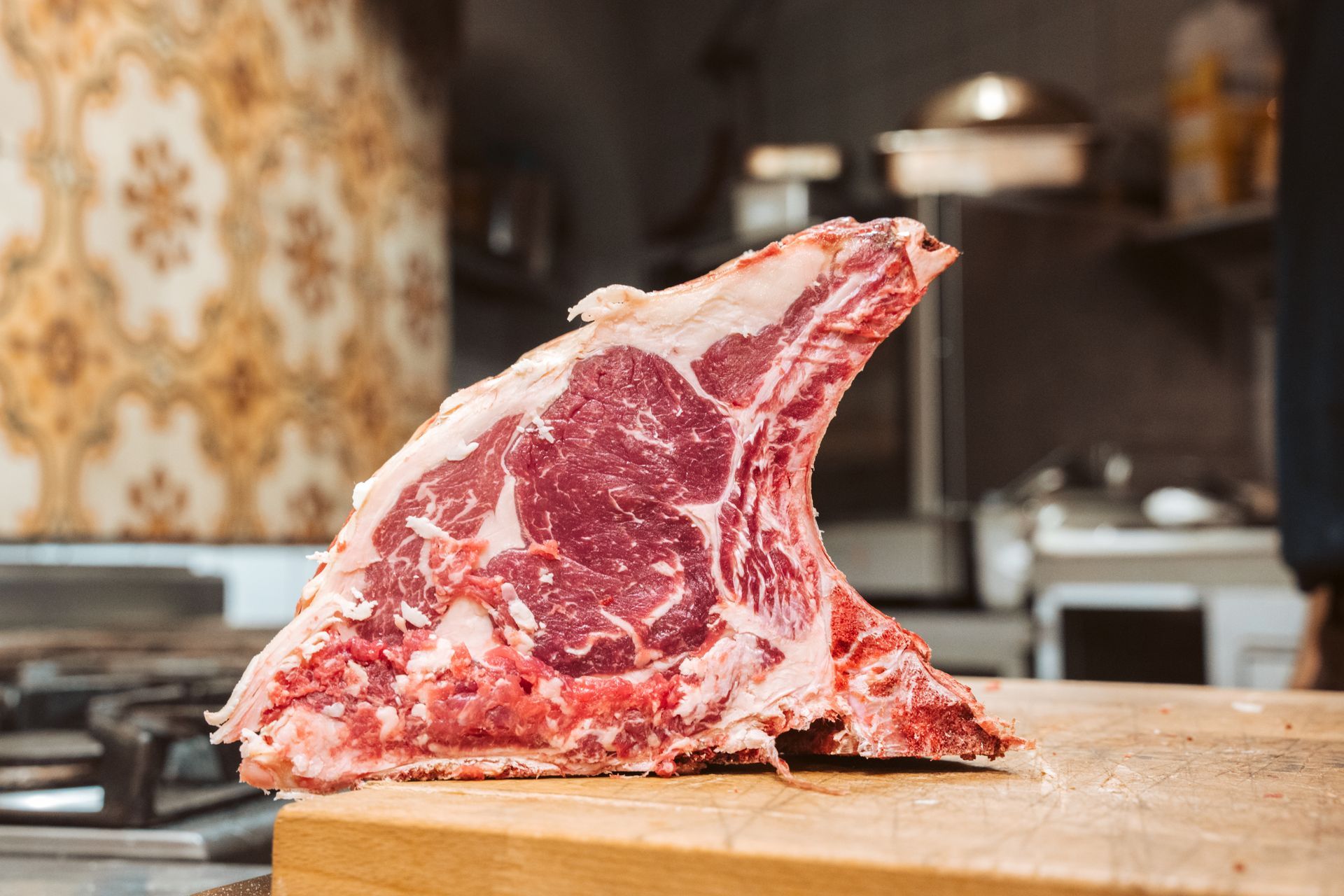 Grande bistecca di ribeye cruda su un tagliere di legno, sullo sfondo della cucina.