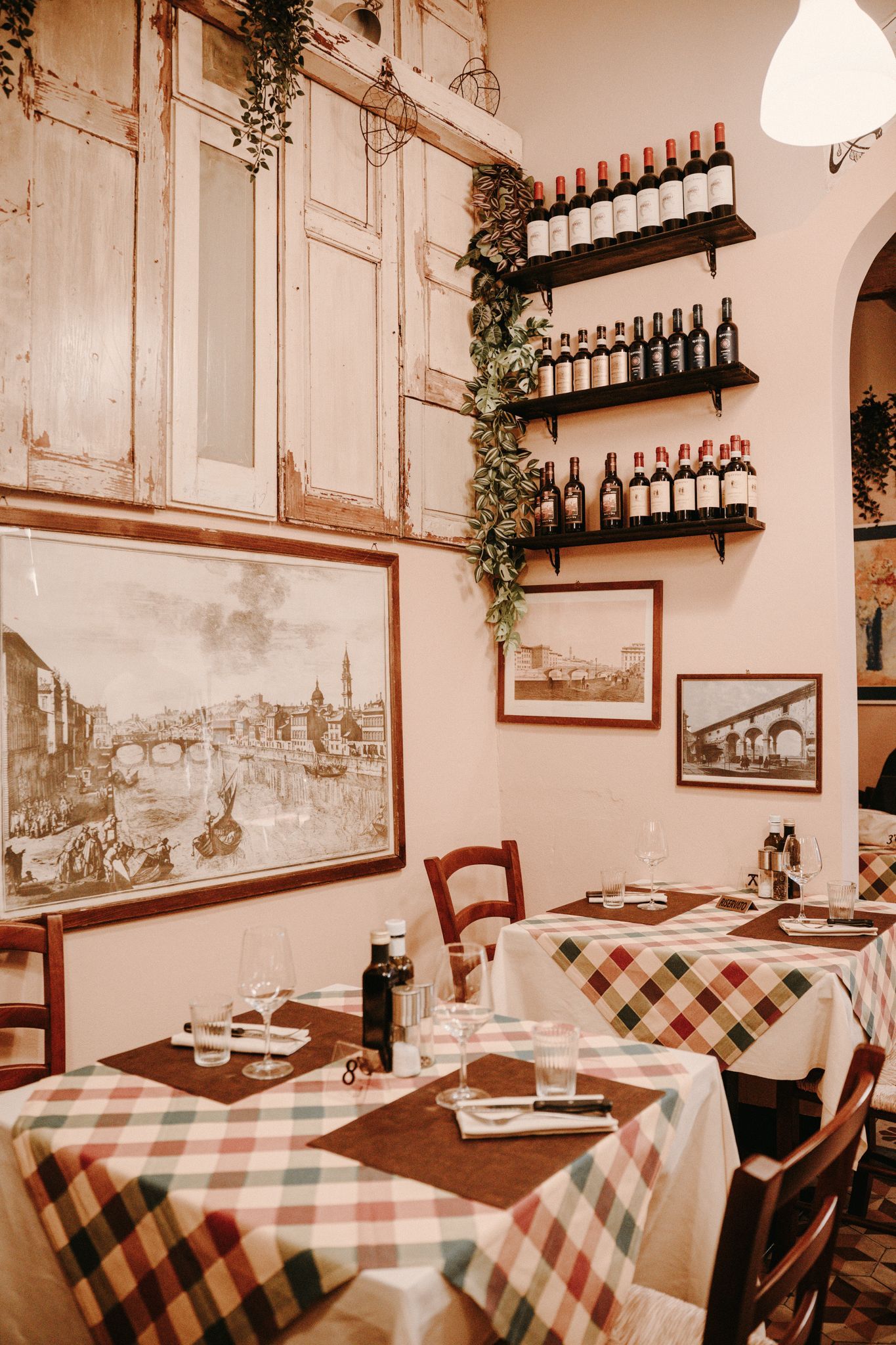 Accogliente ristorante italiano con tavoli, tovaglie a quadri, opere d'arte e bottiglie di vino sugli scaffali.