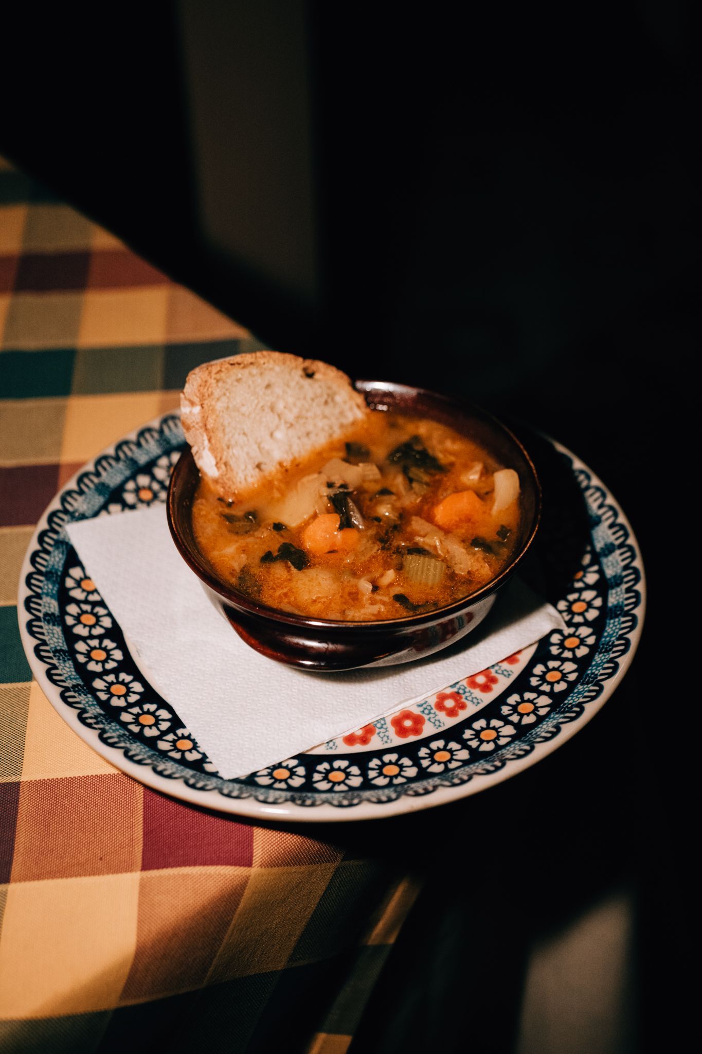 Ciotola di zuppa con pane su piatto decorato, tovagliolo, tovaglia scozzese.