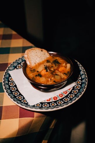 Ciotola di zuppa con pane su piatto decorato, tovagliolo, tovaglia scozzese.