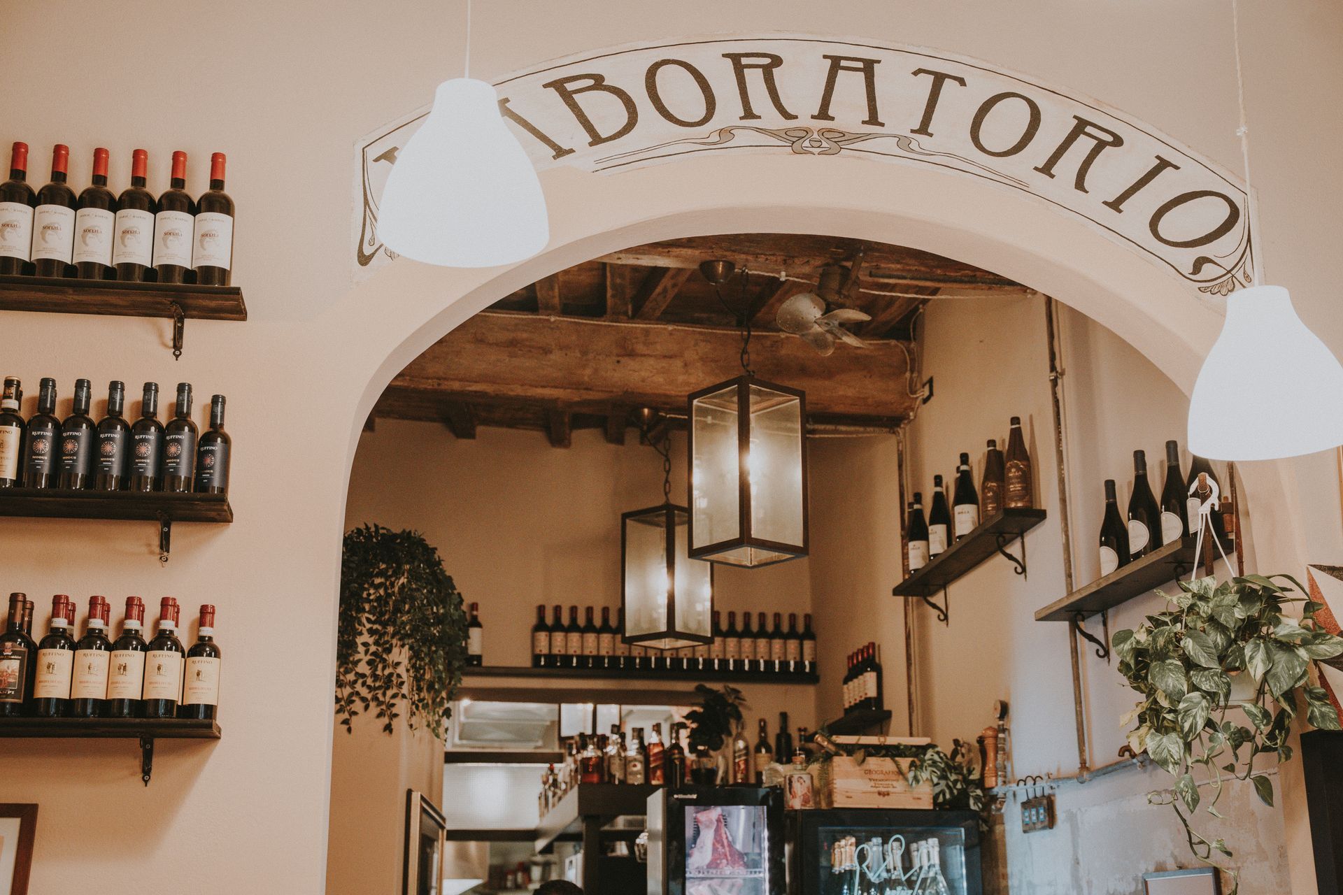 Interno di un'enoteca. Scaffali con bottiglie. Sull'arco è scritto 