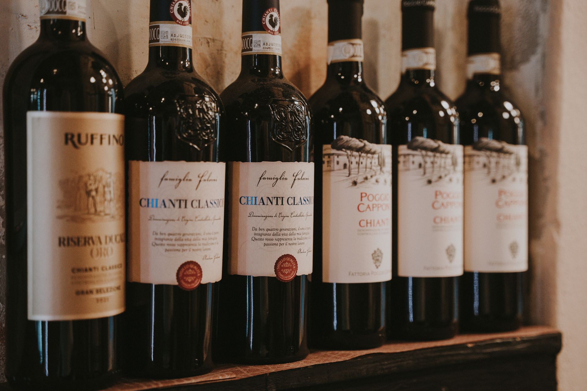 Fila di bottiglie di vino su uno scaffale. Le etichette sono bianche e presentano testo e grafica