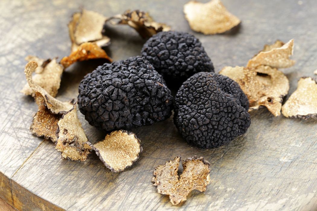 Tartufi neri e fette di tartufo su una superficie rustica in legno.