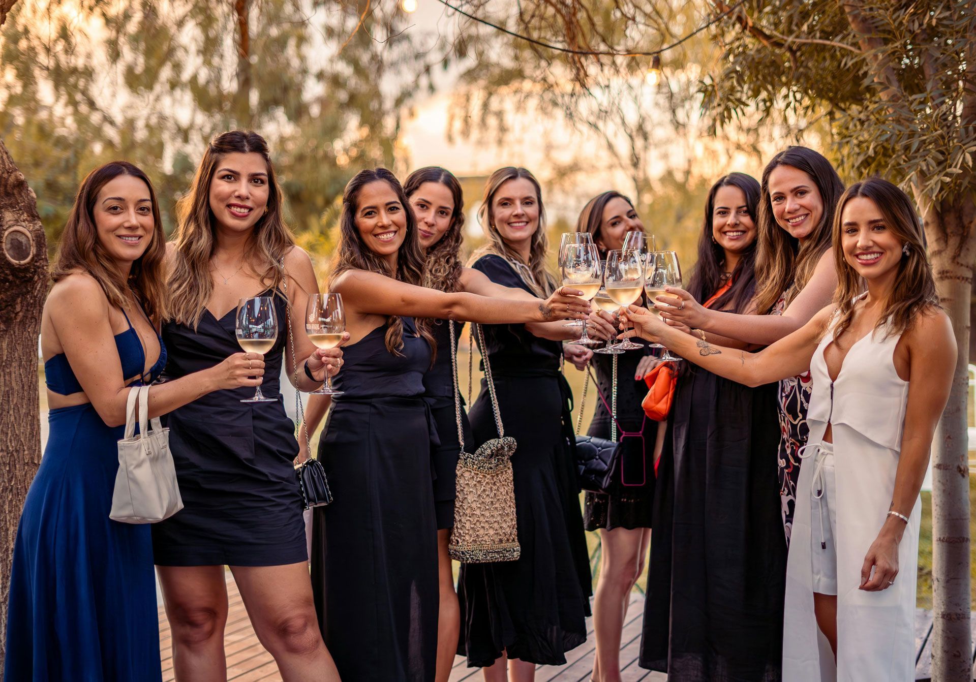 Un groupe de personnes en tenue de plein air trinquent avec des verres de vin dans un espace boisé et ensoleillé.