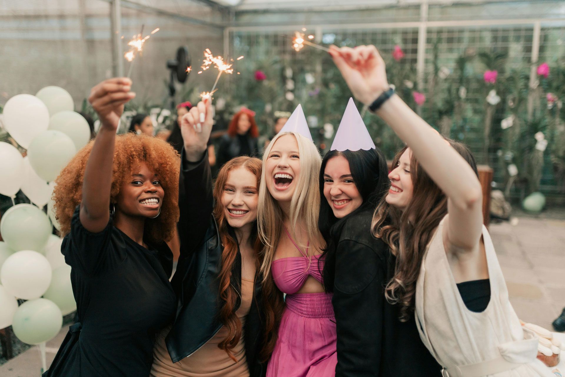 Cinq amis font la fête ensemble à l'intérieur, tenant des cierges magiques et souriant, certains portant des chapeaux de fête.