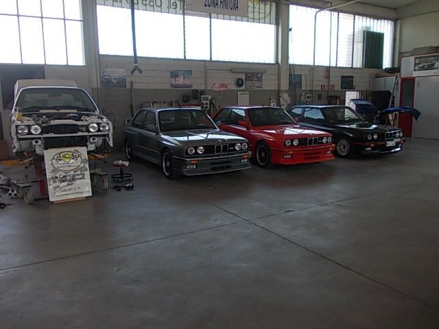 Quattro auto BMW d'epoca in un garage, una delle quali in fase di riparazione, di vari colori.
