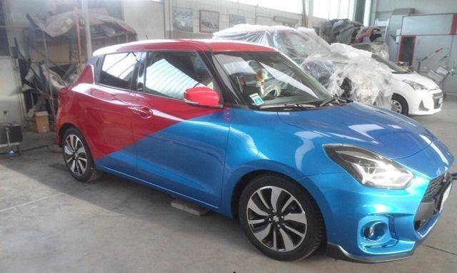 Un'auto Suzuki Swift bicolore rossa e blu parcheggiata all'interno di un'officina.