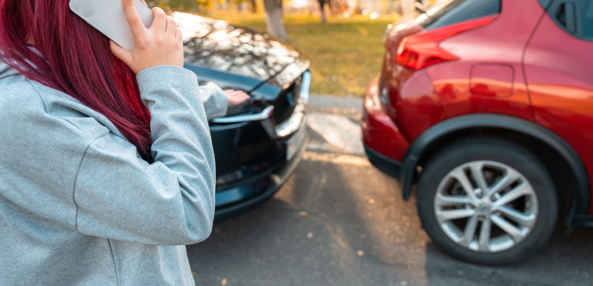 A woman is talking on a cell phone in front of a car accident.