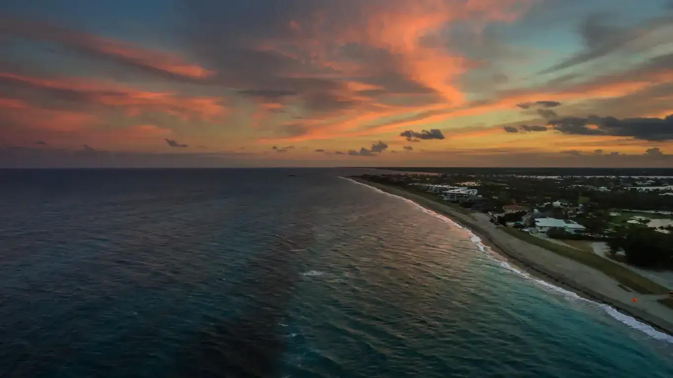 An aerial view of a beach at sunset with a city in the distance.