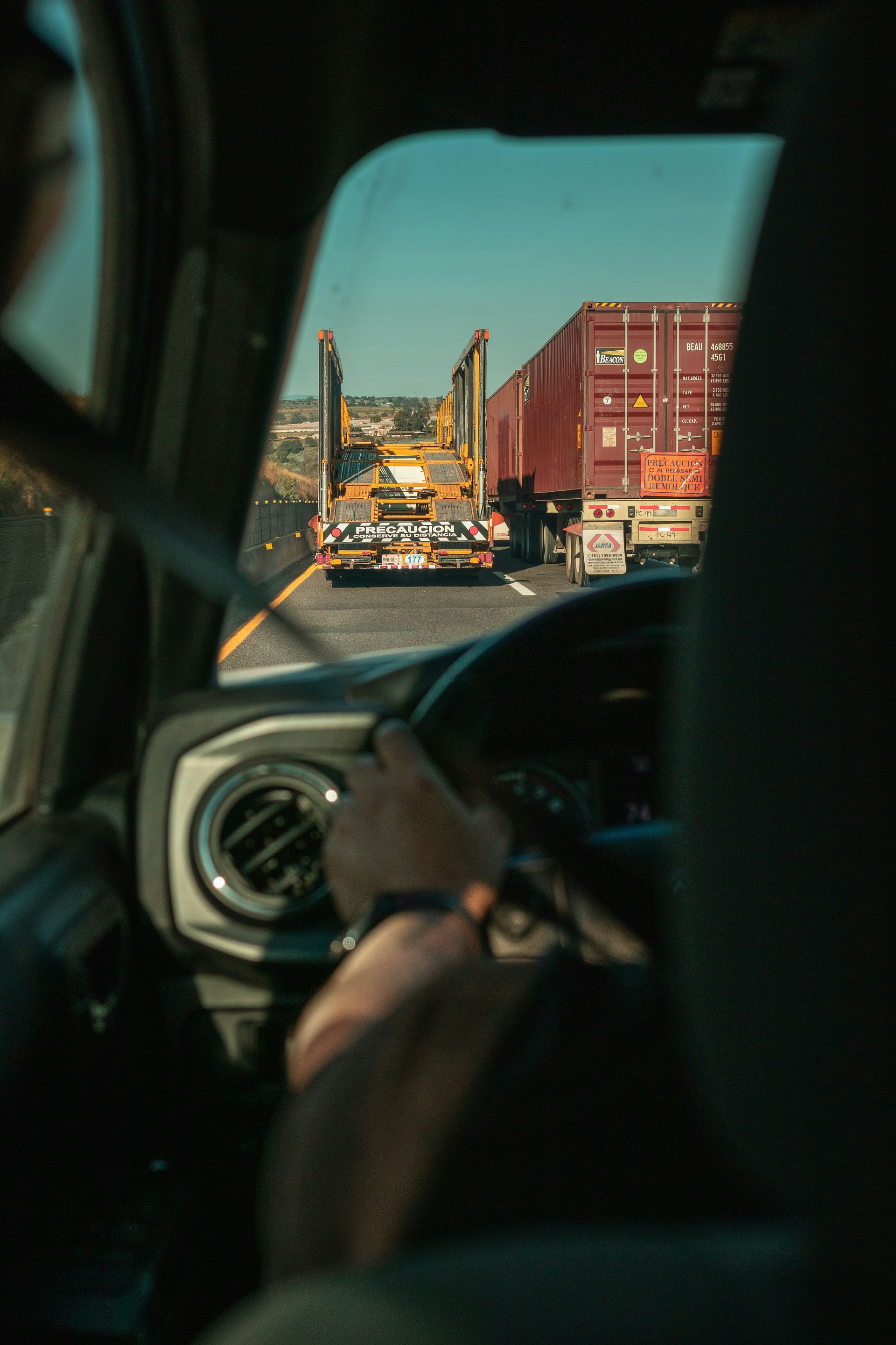 Driver's view from a car of a semi-truck hauling a container on a sunny highway.