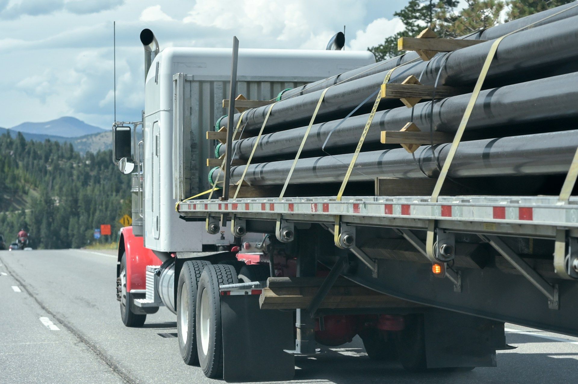 Semi-truck carrying pipes on a flatbed trailer on a mountain road.