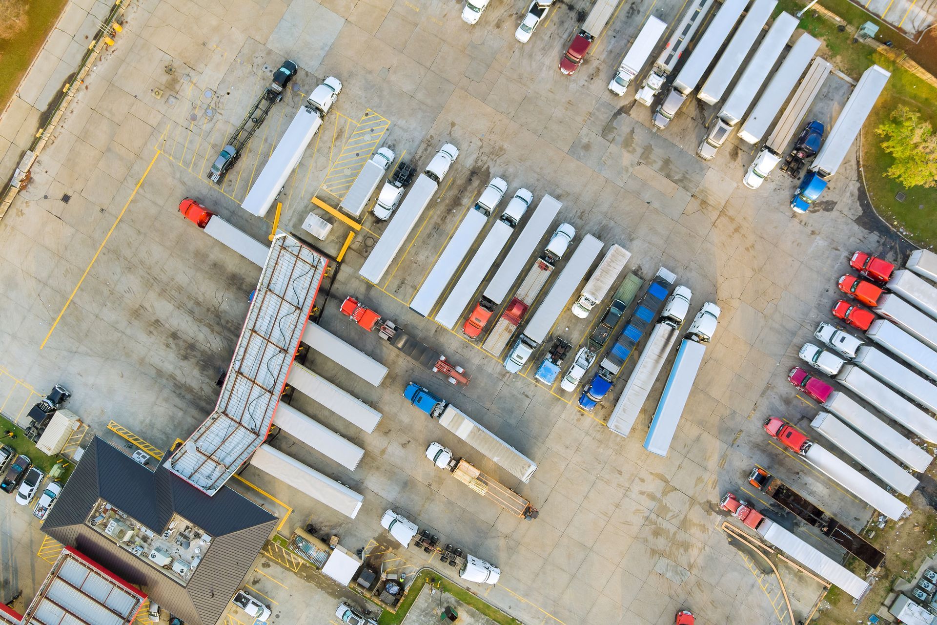 Overhead view of a truck stop with numerous parked semi-trucks and trailers, concrete lots.