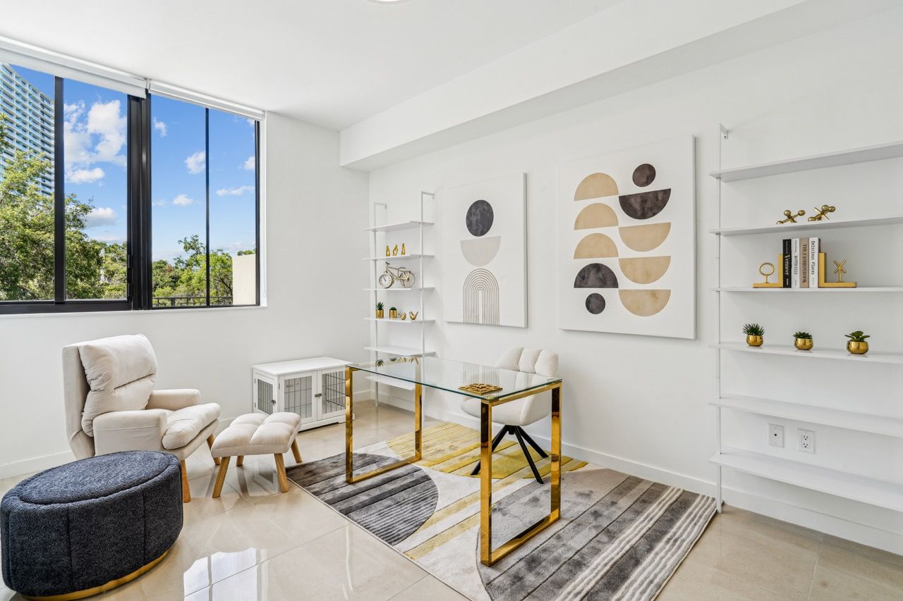 Bright apartment study with a glass desk, white shelving, and abstract wall art.