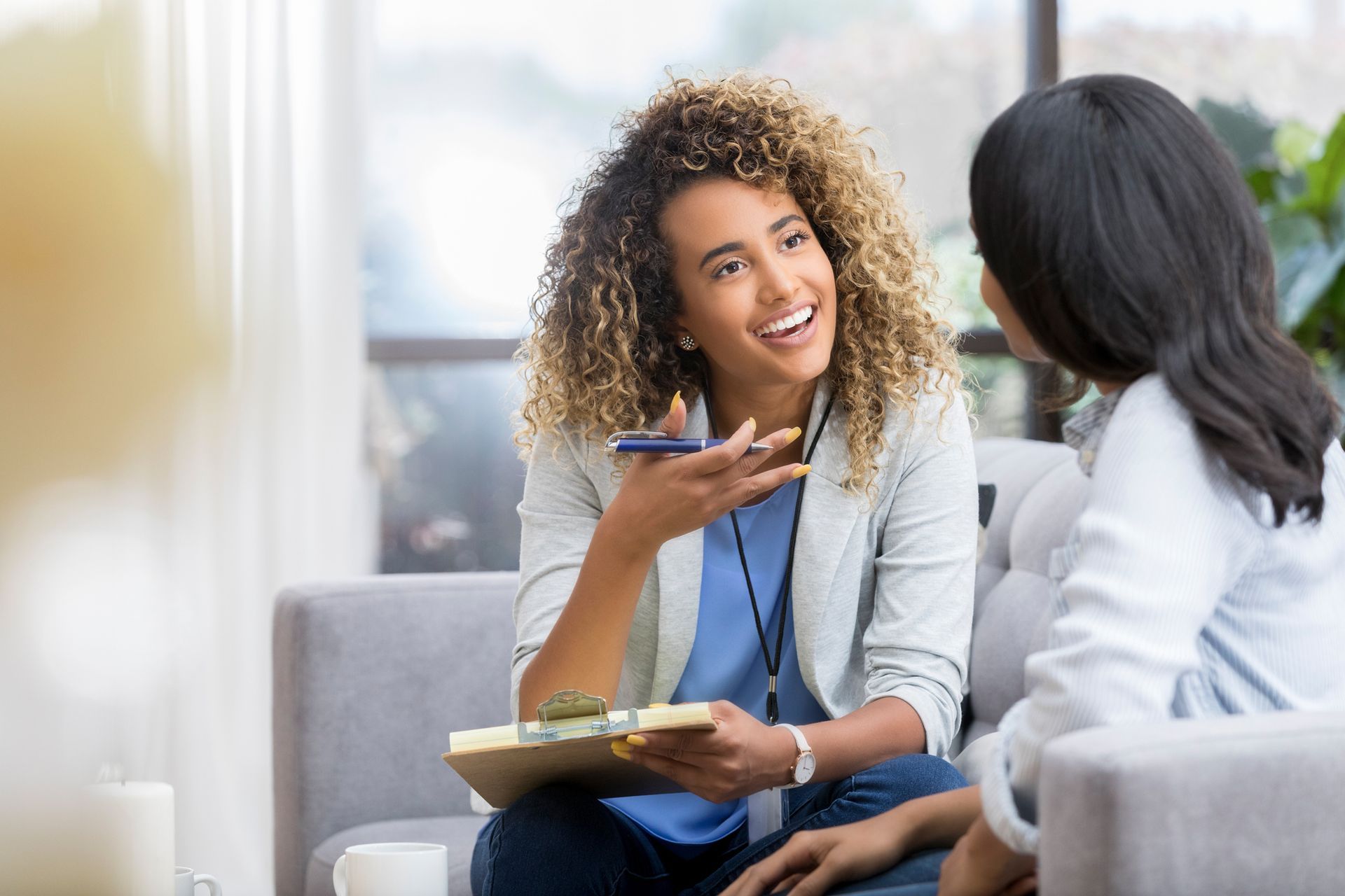 A woman is sitting on a couch talking to another woman.